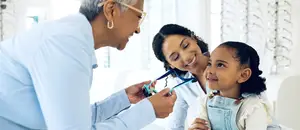 A man is examining a child's eyes with a toy in his hand, and a woman is smiling next to him.