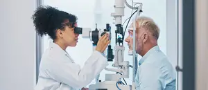 A woman doctor examining an elderly man's eyes with an ophthalmoscope