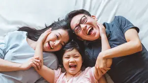 A family of three lying on a bed, smiling and holding hands