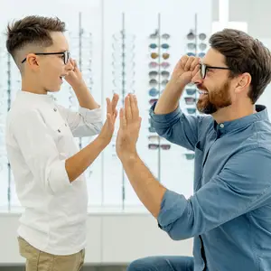 A boy and a man wearing glasses are giving each other a high five in front of a display of glasses.