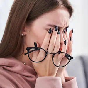 Close-up of a woman wearing glasses and holding her nose with her hands