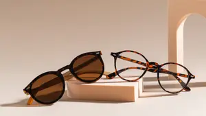 Two pairs of tortoiseshell-framed sunglasses, one with brown lenses and the other with orange lenses, are placed on a beige platform with a shadow cast on it.