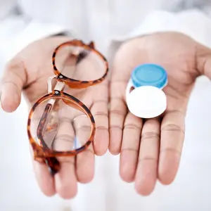 An adult person is holding a pair of glasses and a small bottle of eye drops in their hands