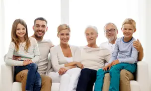 A family of six is sitting on a couch in a living room, posing for a picture with smiles on their faces.