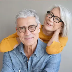 A smiling elderly man and woman are posing for a picture while standing close to each other