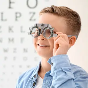 A young boy is holding a pair of glasses with lenses in front of an eye chart.