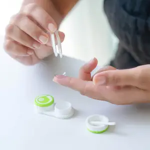 A woman is putting on a contact lens using tweezers.