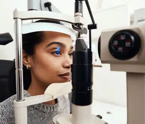 A woman is examining her eyes using an ophthalmoscope in a medical setting.