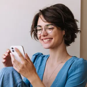 A woman in a blue shirt is smiling and looking at her phone.