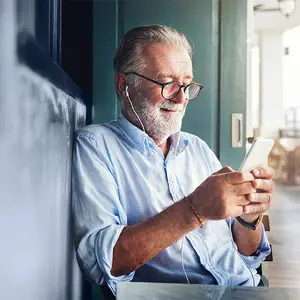 Older man wearing glasses and headphones listening to music on his phone.