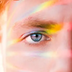 A close-up view of a person's eye with a rainbow-like color around it.