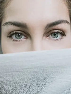 Close up of a woman's face with eyes looking over a white cloth.