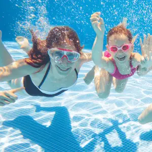 Three children wearing goggles are swimming and playing in a swimming pool.