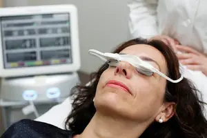 A woman is lying on a bed wearing an eye mask with a monitor in front of her