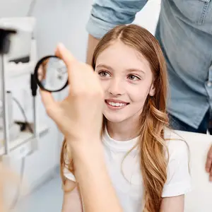 a girl is sitting in a chair and having her eye examined by a doctor
