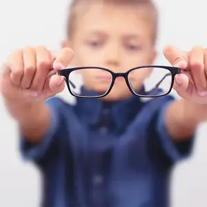 A boy with glasses is holding them in both hands and looking at them