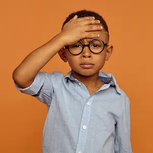 A young boy with glasses covering his eyes with his hand
