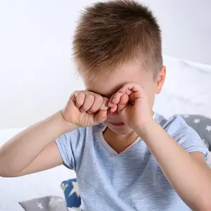 A young boy with brown hair is covering his eyes with his hands, possibly feeling sad or upset.