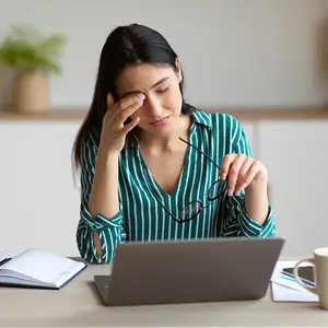 woman sitting at a desk with a laptop rubbing her forehead