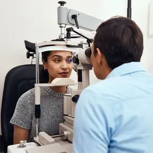 A woman is sitting in a chair and having her eyes examined by a man wearing a blue shirt.