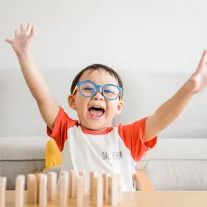 A boy wearing glasses and raising his hands while playing a game of Jenga
