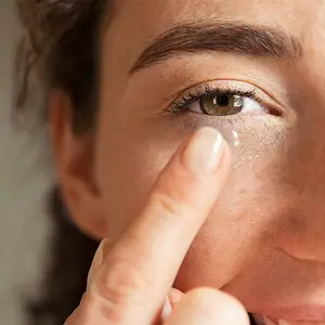 A woman is putting on a contact lens in her left eye