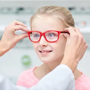 A young girl tries on red glasses while a doctor adjusts them for her