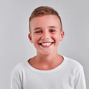 A young boy wearing a white t-shirt is smiling for a photograph against a gray background