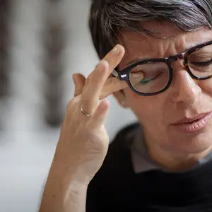 A woman wearing glasses adjusting them on her face while looking down.