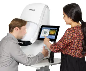 A man and a woman are standing in front of a Nikon optos device with a screen displaying an eye image