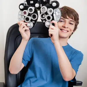 A boy is holding an eye chart with a smile on his face while sitting on a chair.