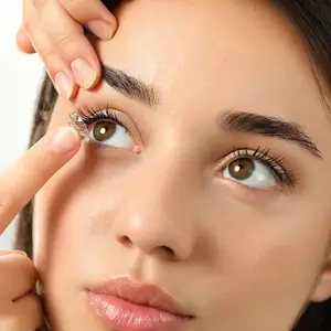 A woman carefully placing a contact lens on her eye, likely in a clinic or medical setting.