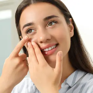 A woman with brown hair and a striped shirt is smiling and holding her fingers near her eyes.