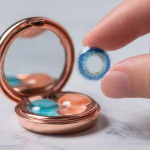 A person is holding a blue and white contact lens in their hand in front of a mirror.