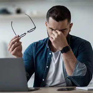 Man with blurry vision adjusting his glasses while working on a laptop