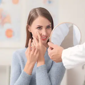 woman trying on a contact lens and smiling at herself in a mirror