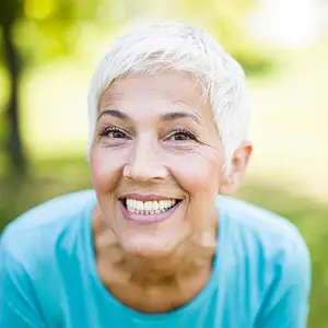 Elderly woman with white hair and a blue shirt is smiling in a park