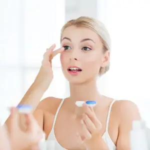 A woman is adjusting her contact lens in front of a mirror