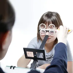 A girl is having her vision tested by an optometrist wearing glasses and holding a pencil.