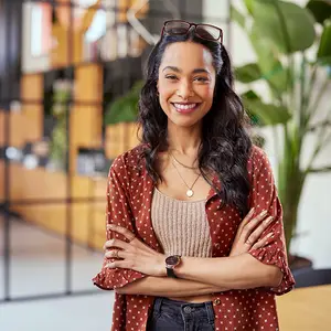 Portrait of a woman smiling at the camera while standing with her arms crossed in an office.