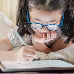 Asian girl in glasses lying in bed drawing on a tablet