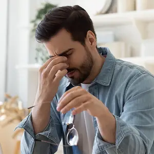 Man holding his head in pain and looking at his glasses