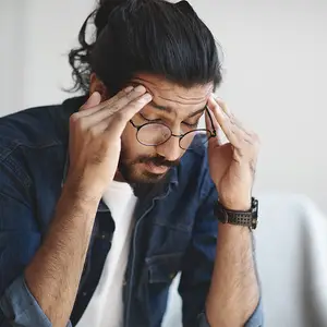 Man with glasses touching his forehead with his hands in a thoughtful pose