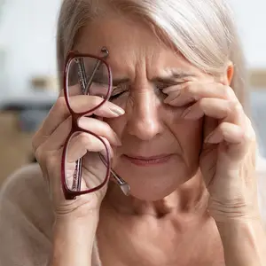 an older woman holding her eyes and crying while holding a pair of glasses
