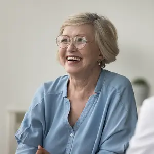Elderly woman wearing glasses smiling and talking to another person