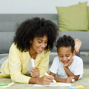 A woman and a boy lying on the floor drawing and coloring on paper with markers and crayons