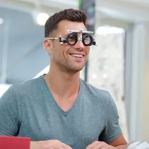 A smiling man wearing a gray V-neck shirt and a pair of glasses with a black frame and black lenses is looking at something while sitting in front of a glass wall.