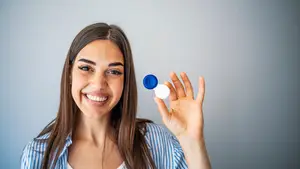 A woman is holding a blue and white contact lens case and smiling