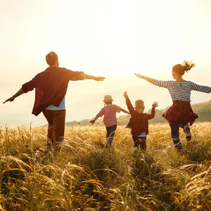 A family of four is running across a tall grass field during sunset.