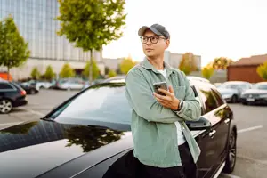 A man in a parking lot checking his phone by his car